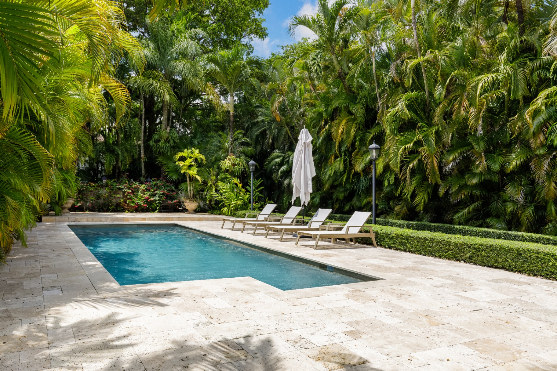 Aerial view of a private garden estate with a turquoise swimming pool framed by palms, bougainvillea, and lounge cabanas
