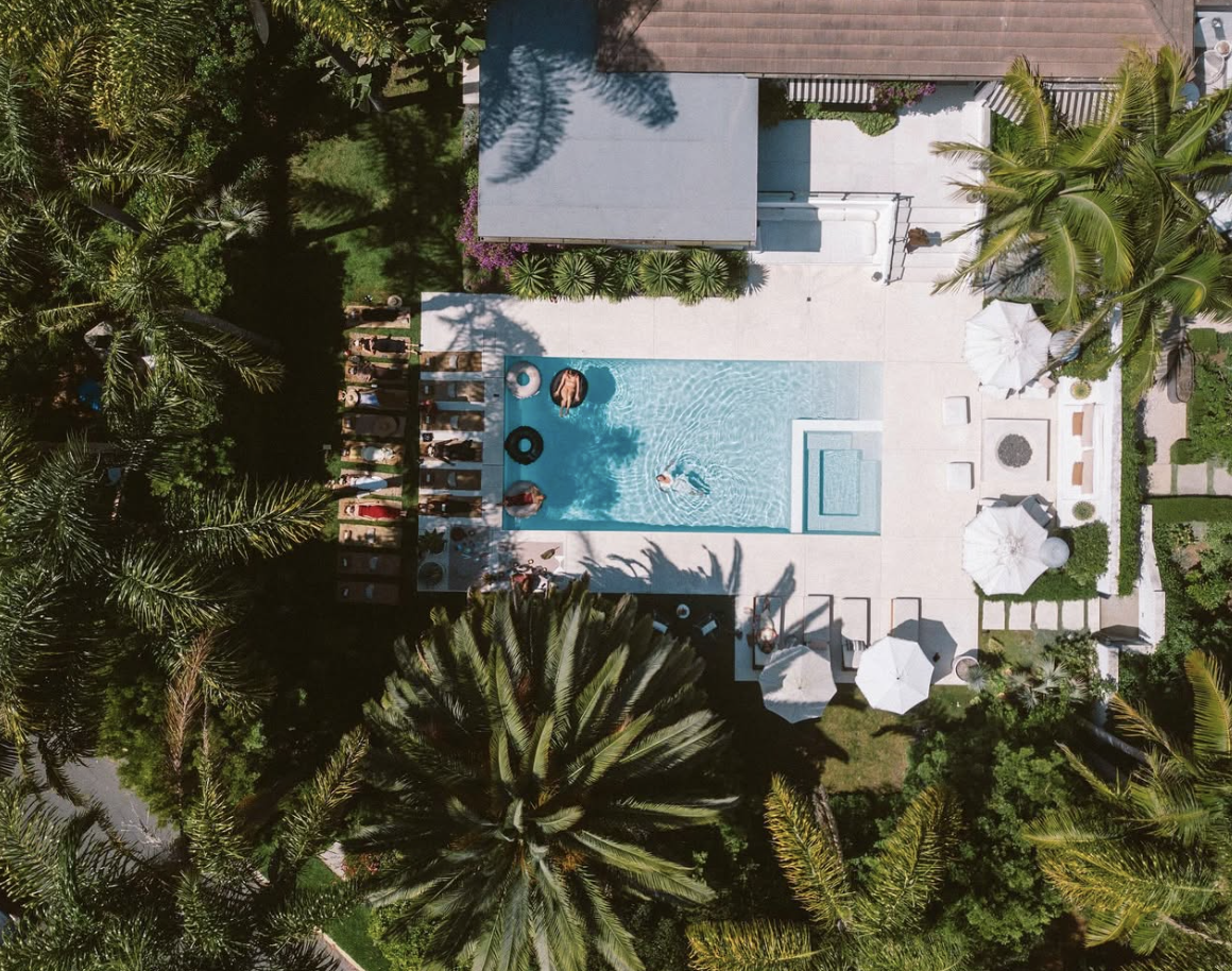 Aerial view of a private estate with a turquoise pool surrounded by lush palms and manicured grounds